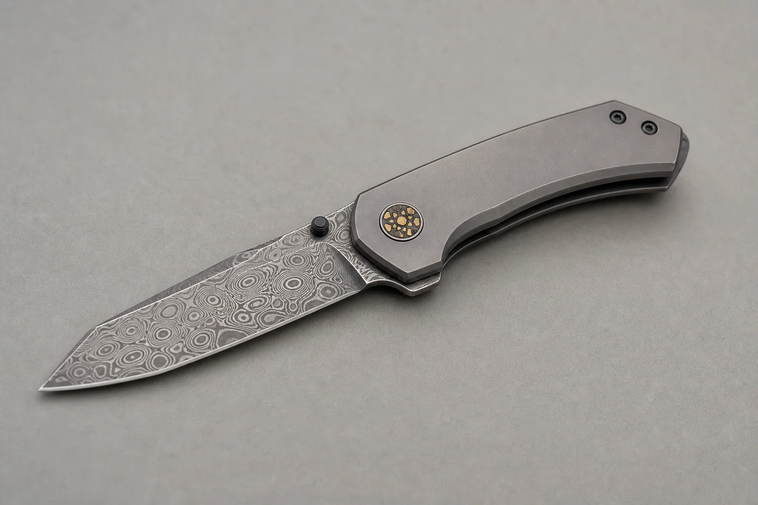 Premium folding knives with titanium handles and Damasteel blades on a dark slate surface