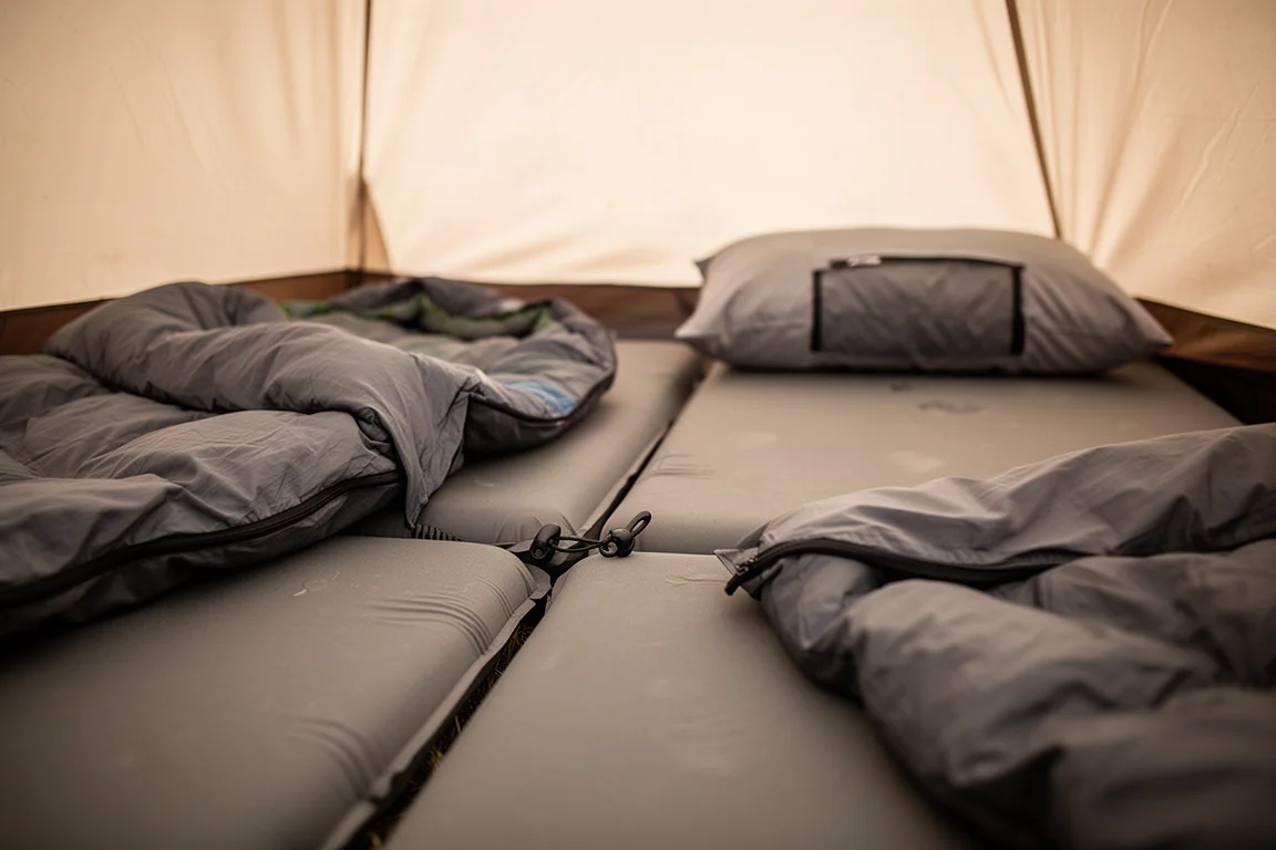 Deux grands matelas de couchage réunis par des attaches dans une tente avec des sacs de couchage par-dessus