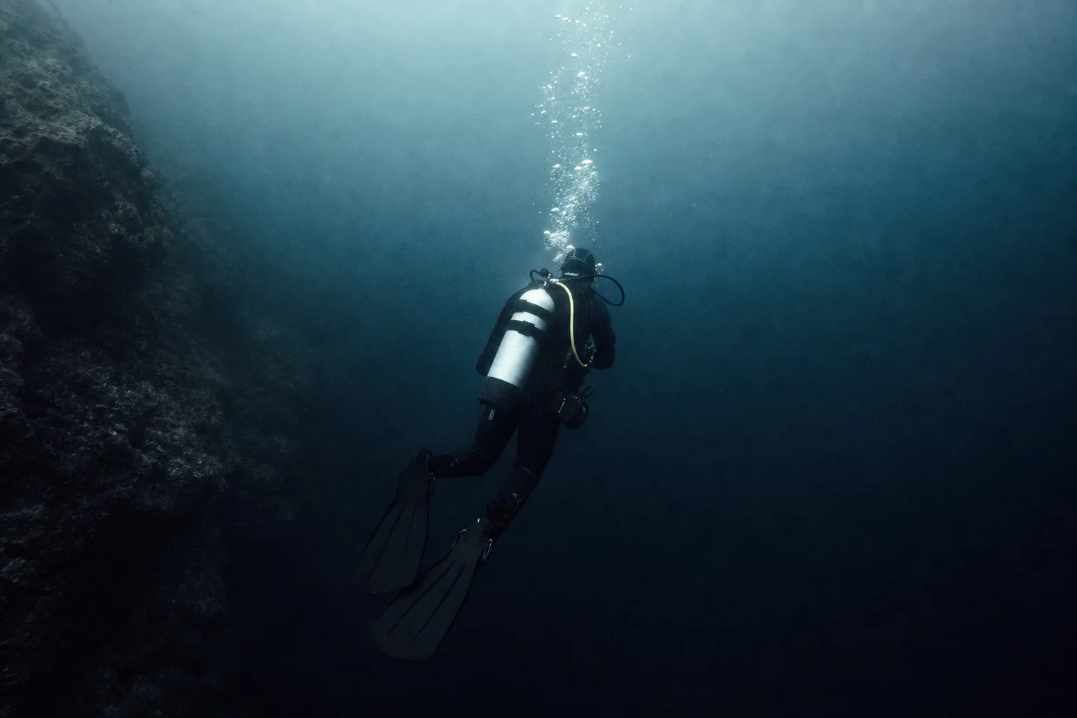 Scuba diver descending into cold dark water with complete regulator setup