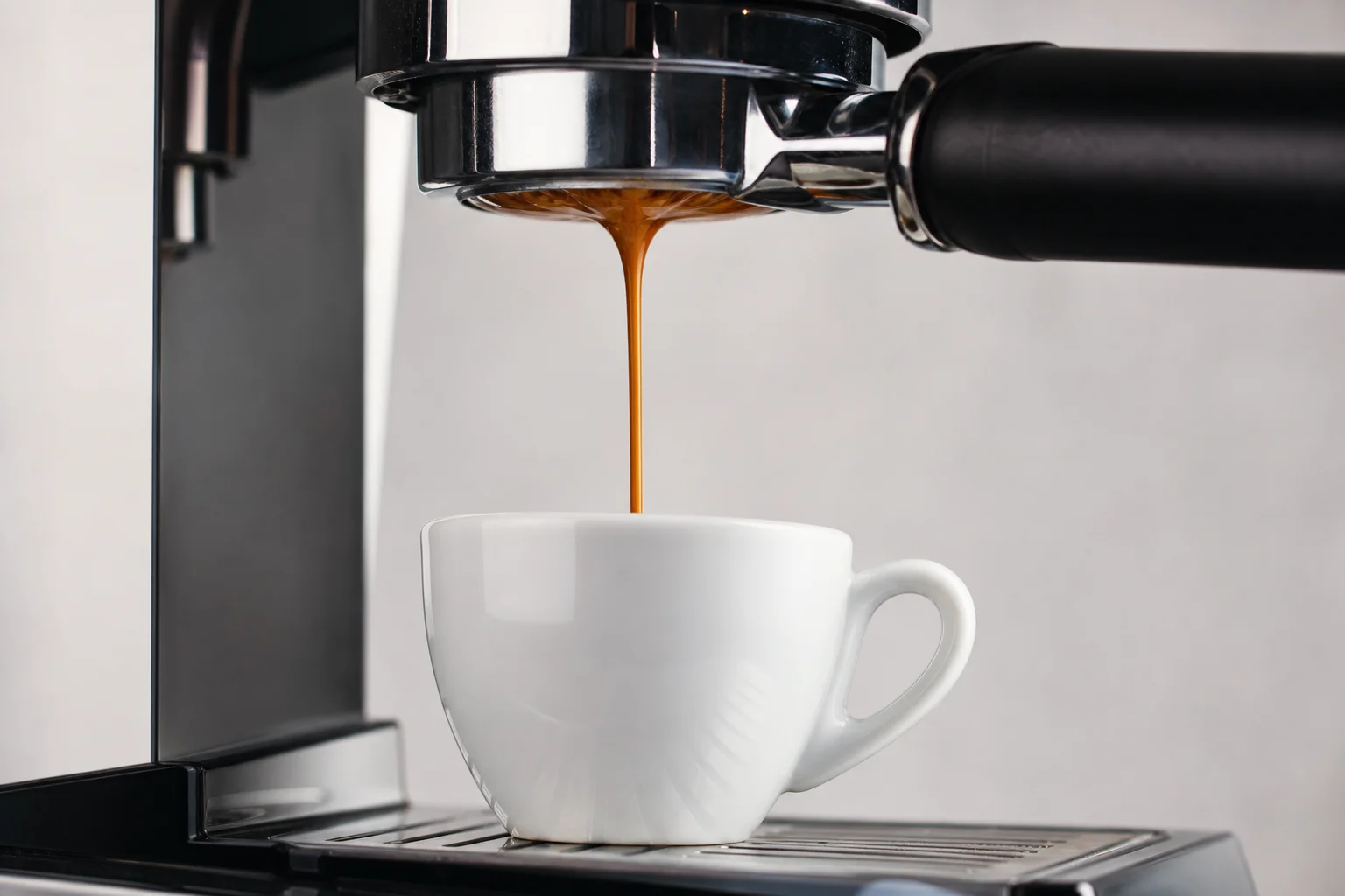 Espresso extraction pouring from portafilter into white cup