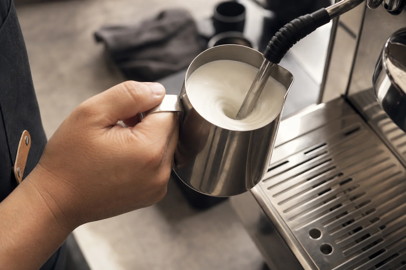 Barista steaming milk in a metal pitcher with a steam wand, creating a whirlpool
