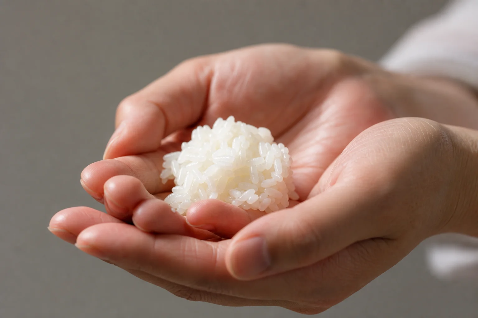 Hands holding freshly cooked sushi rice with individual grains visible