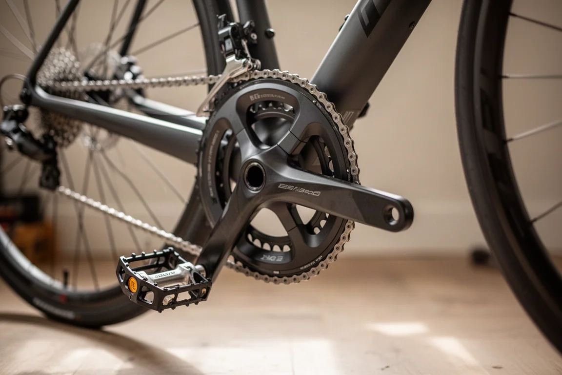 Road bike crank arms with pedal installed, ready for setup on a home workshop floor