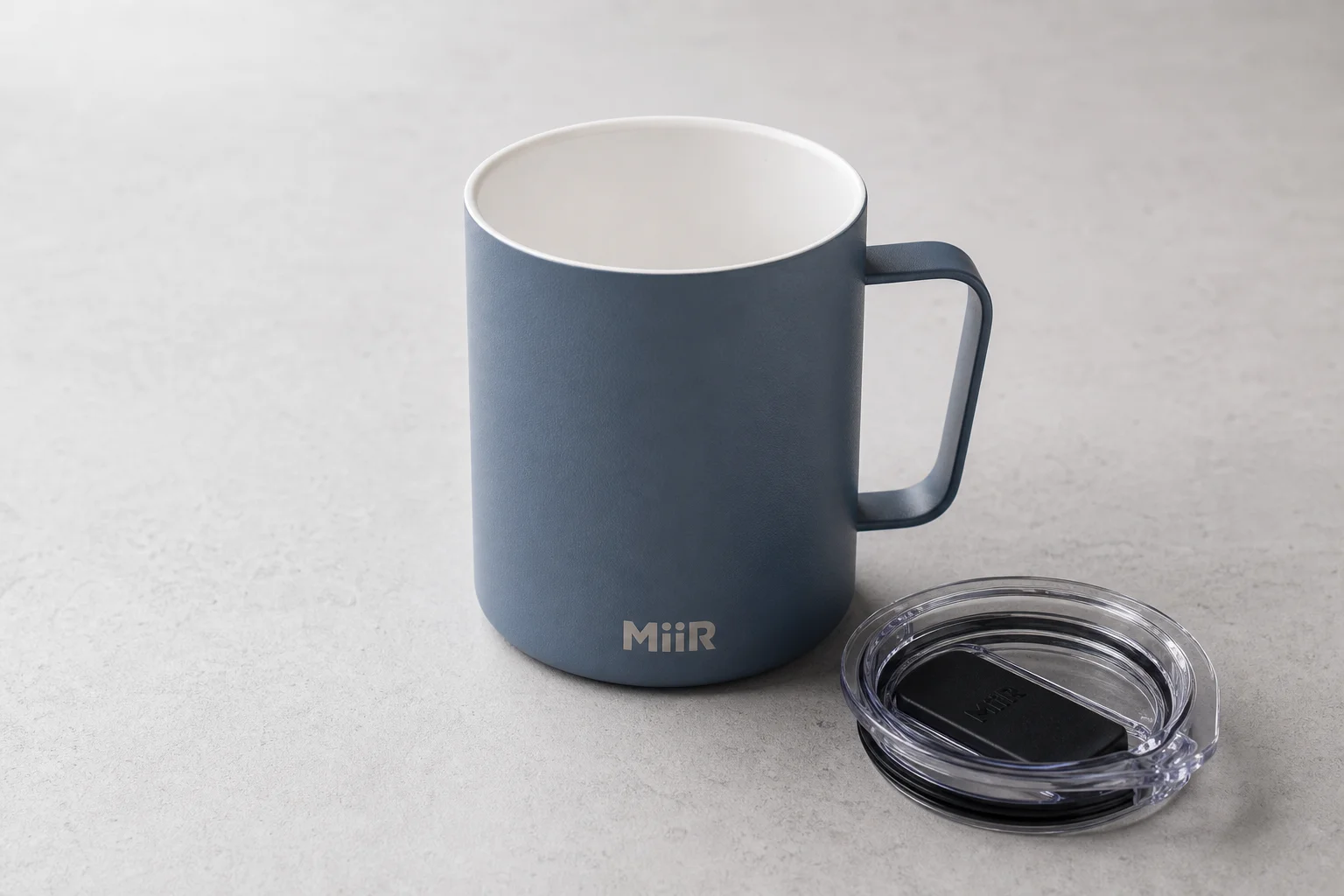 Acht wiederverwendbare Kaffeebecher auf einer Betonoberfläche, die eine Vielfalt an Materialien und Designs zeigen