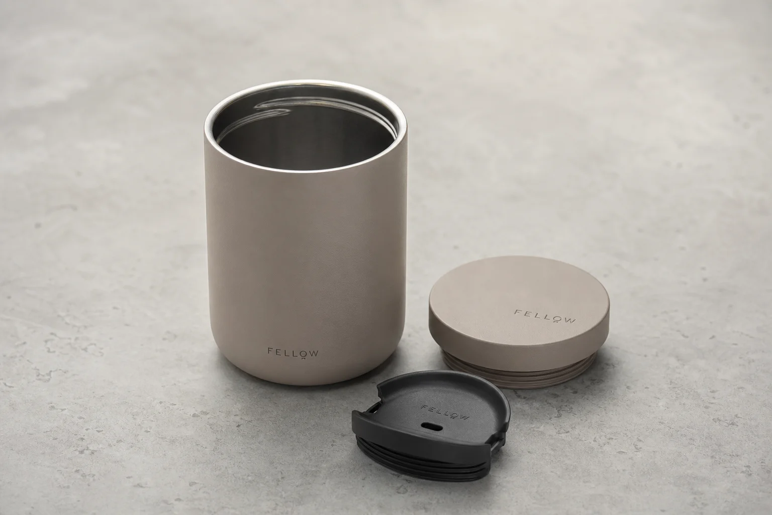 Nine insulated travel mugs arranged on concrete surface in various styles and colors