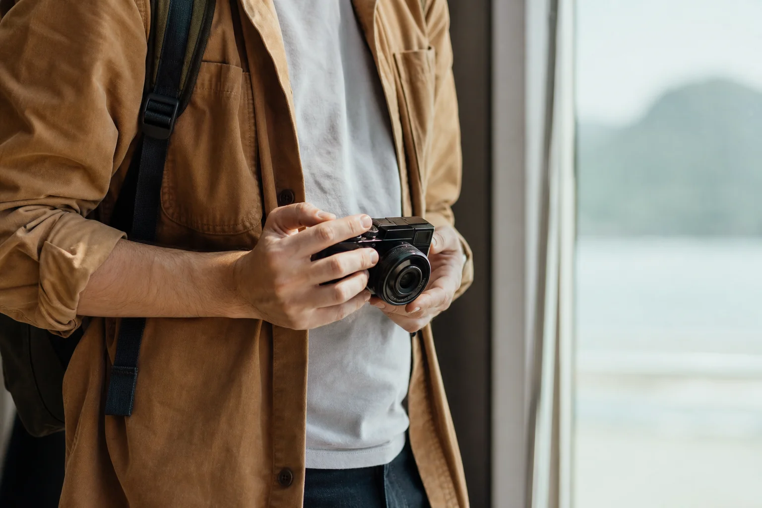 Photographer holding compact mirrorless camera with interchangeable lens outdoors