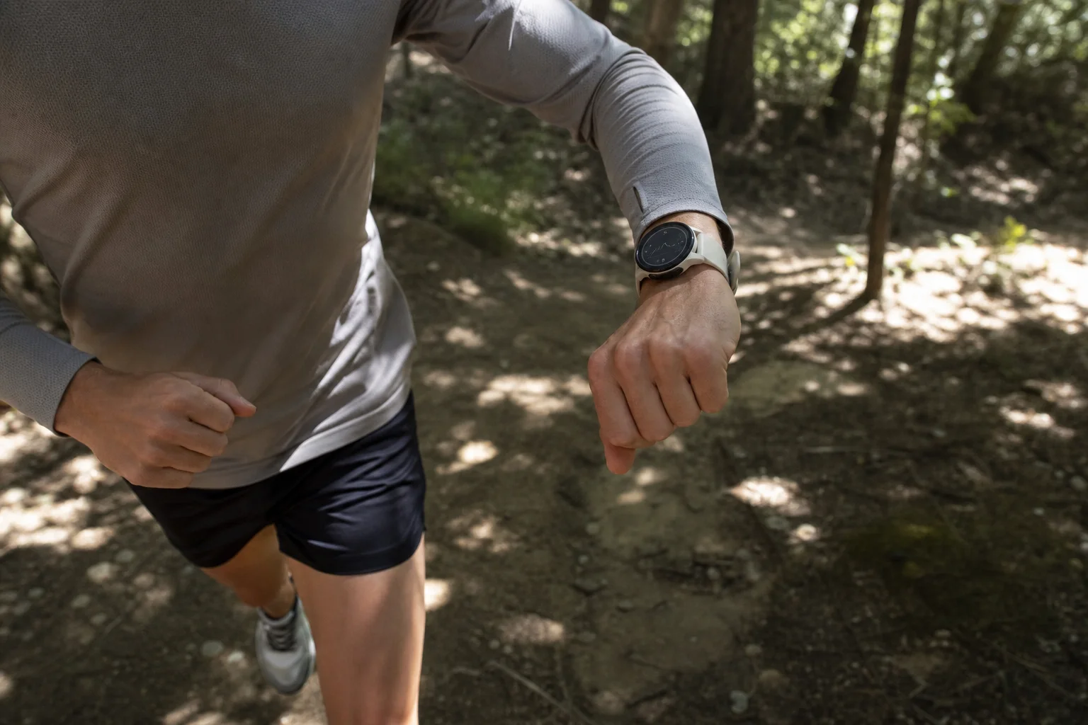 Läufer auf einem Trail prüft Tempo- und Distanzdaten auf einer Sportuhr