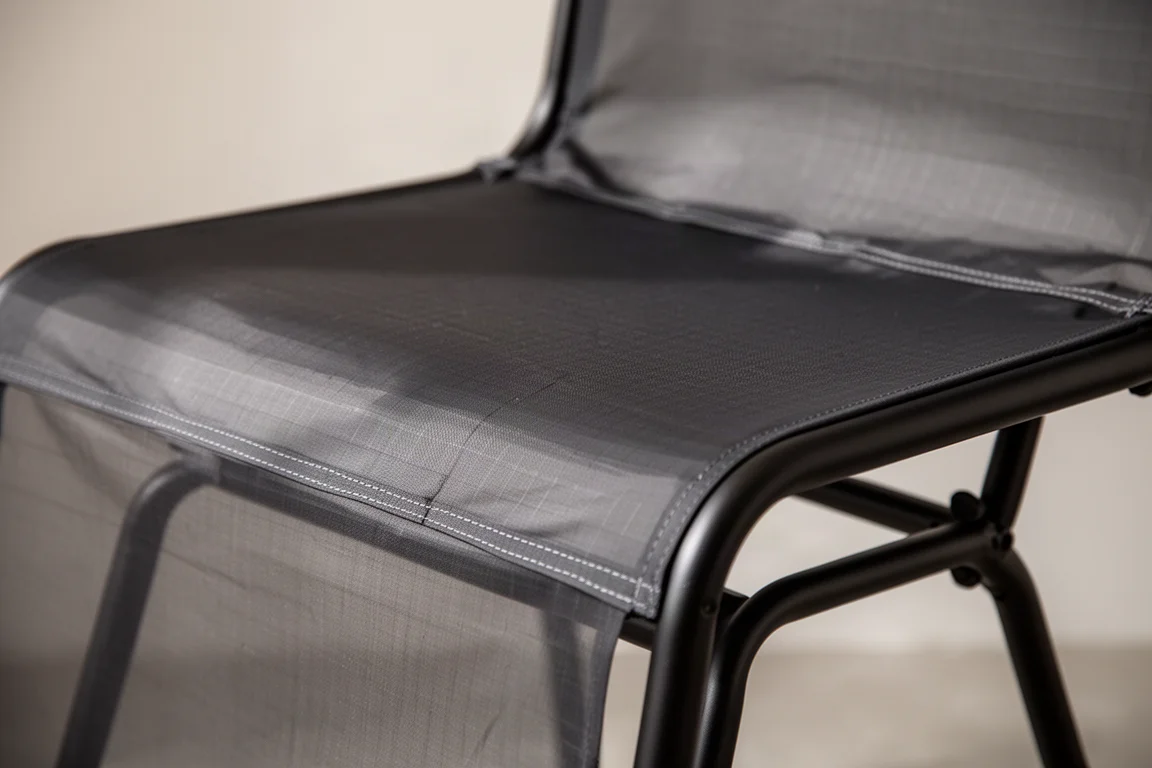 Primer plano de la tensa tela de asiento de ripstop oscura estirada sobre el armazón de acero de una silla