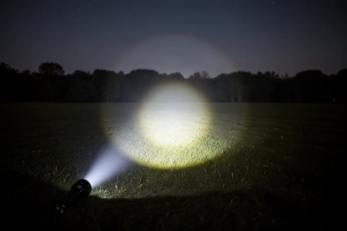 Breiter Außenlichtkegel einer Taschenlampe, der nachts ein dunkles Feld ausleuchtet