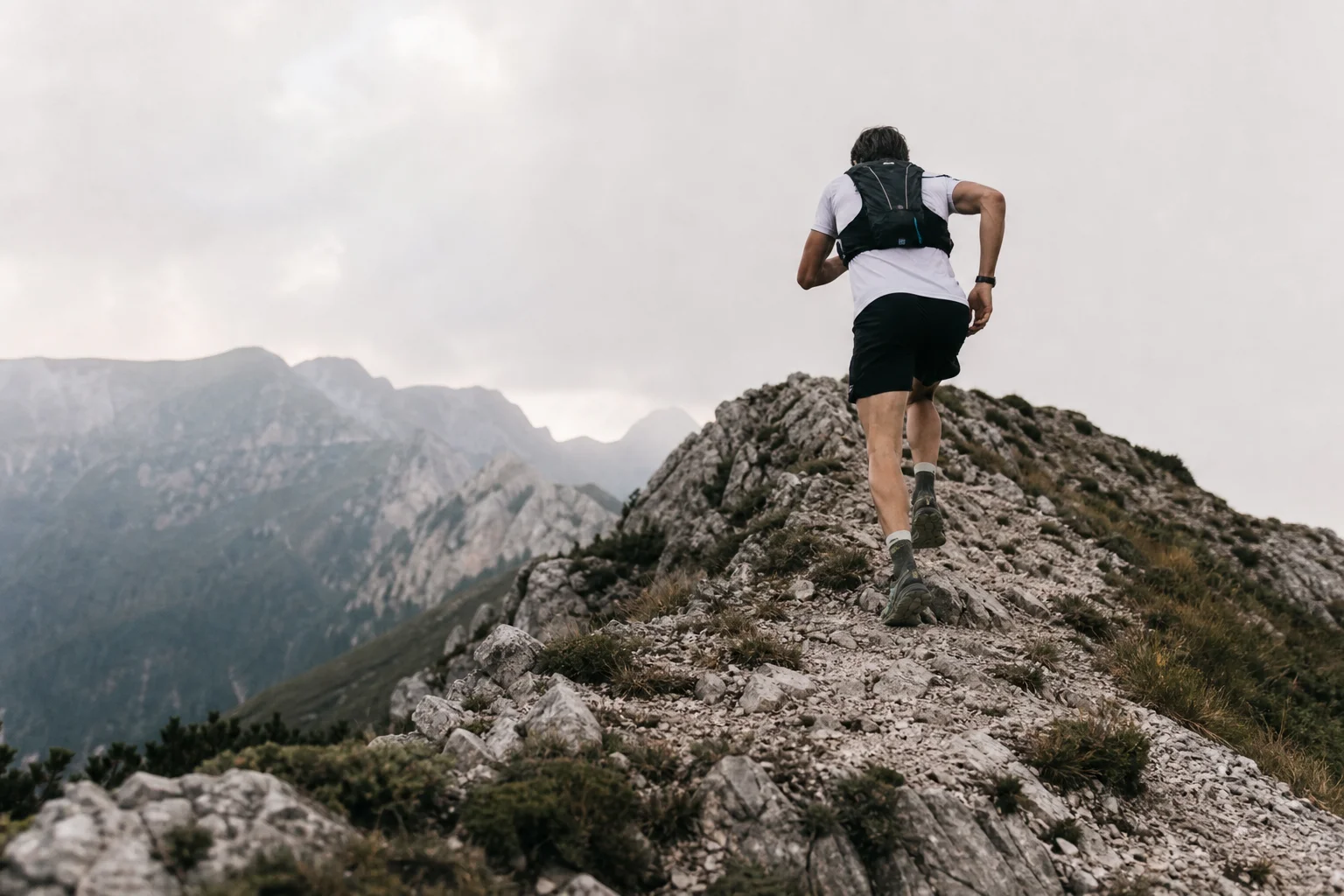 Traileur montant une crête de montagne abrupte avec un gilet d'hydratation