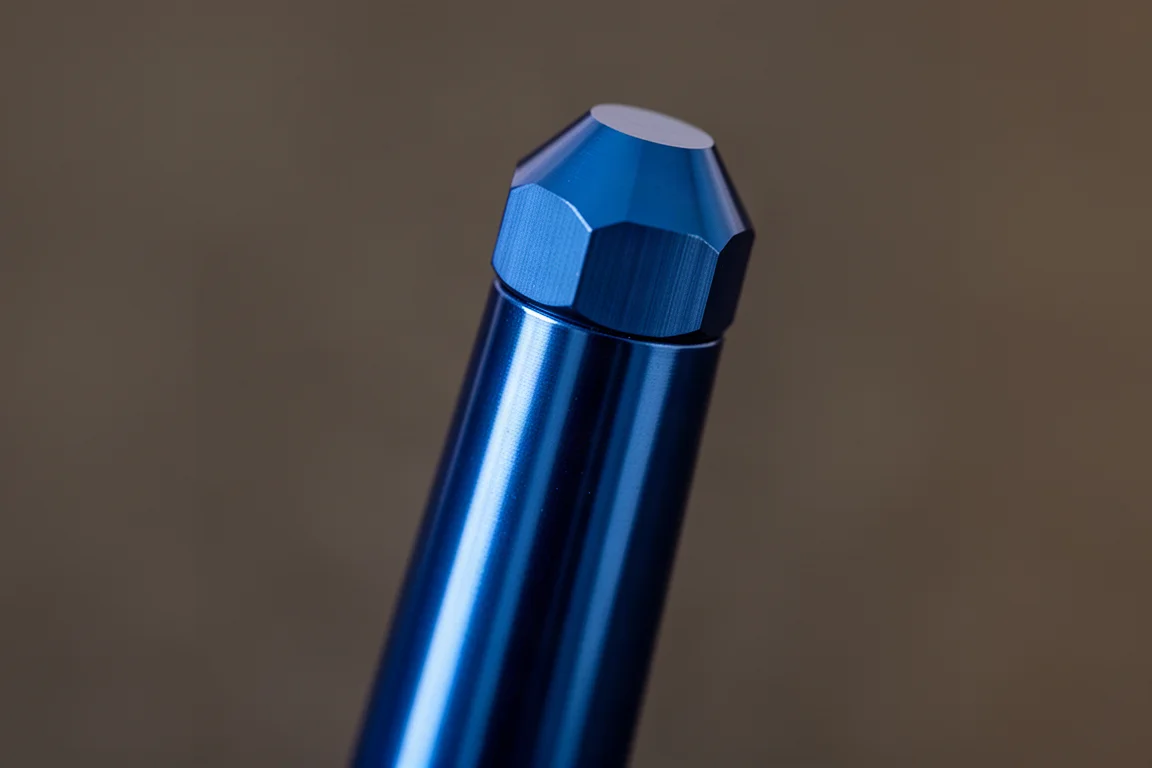 Närbild på ett fasetterat pennlock och en avsmalnande aluminiumkolvar i mjukt ljus