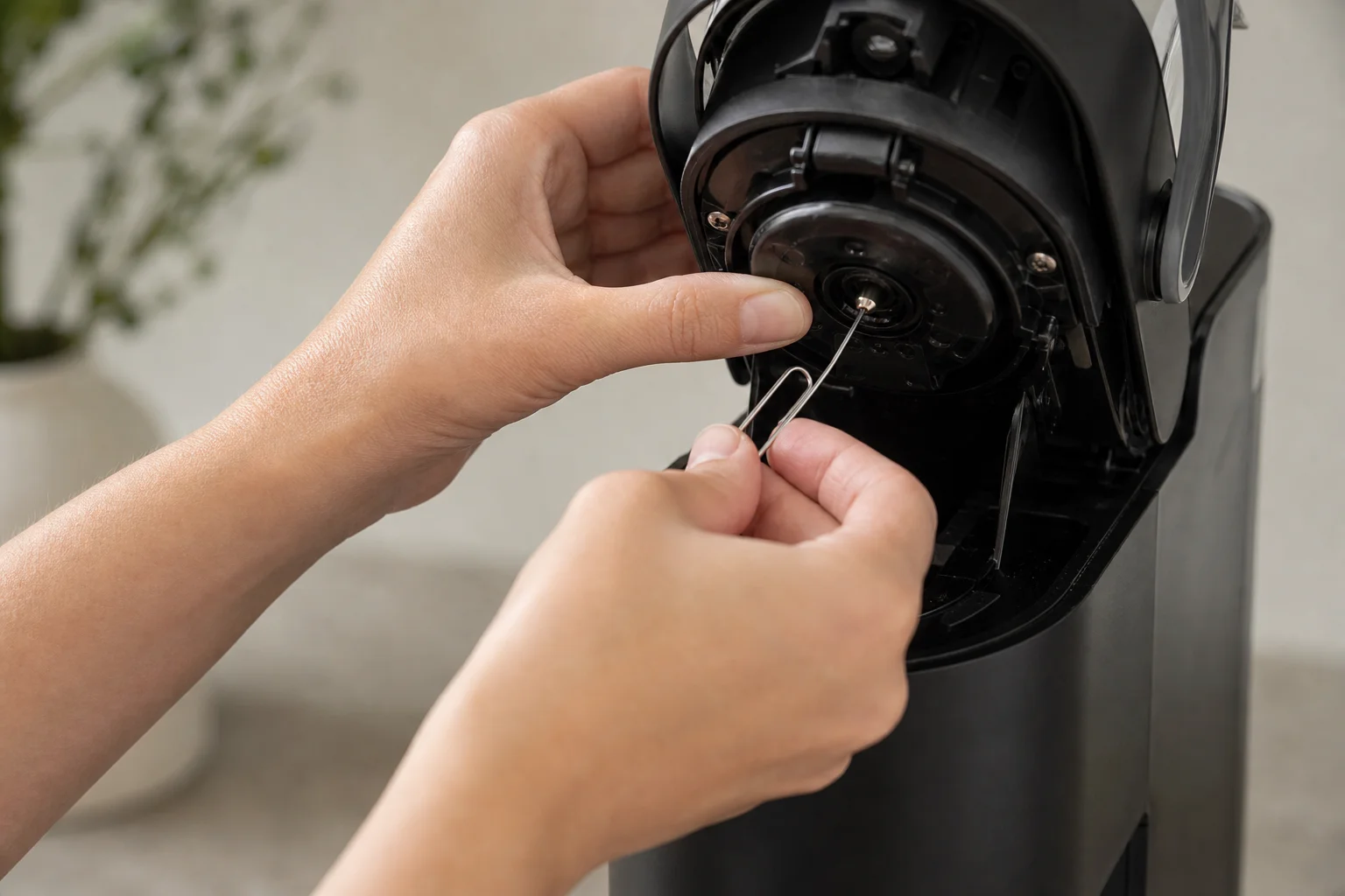 Hands performing maintenance on Keurig needle with paper clip tool