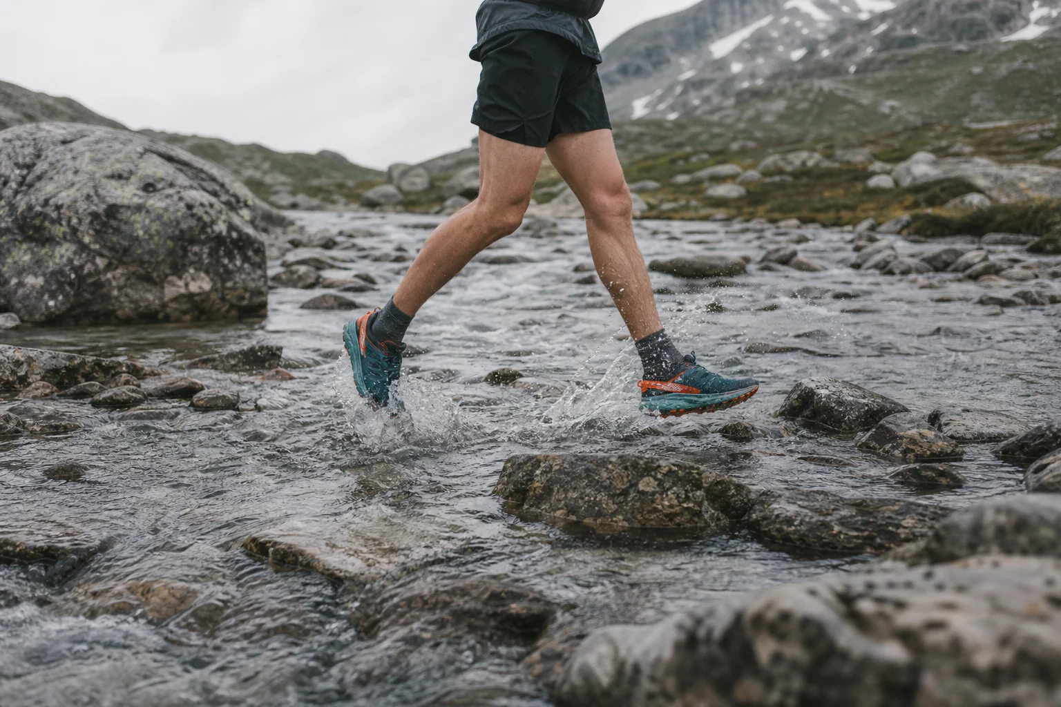 Trail runner crossing a rocky creek bed with water splashing around shoes