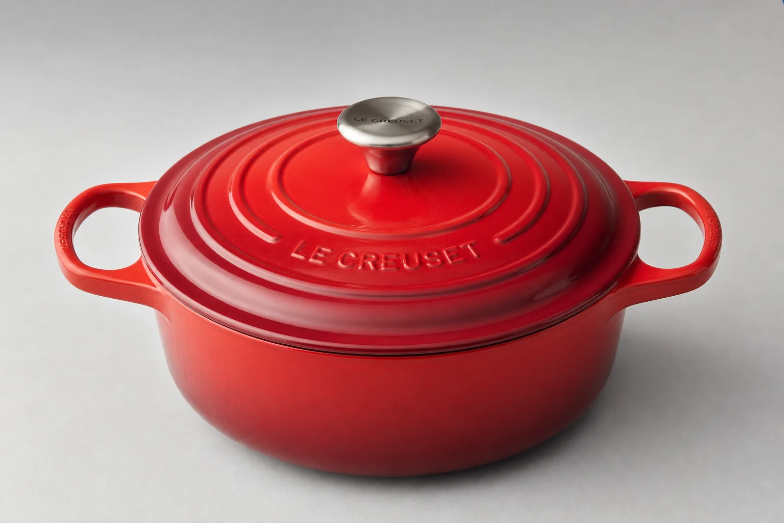 Tre stycken Dutch ovens i färgerna vinröd, gräddvit och röd uppställda på en betongyta