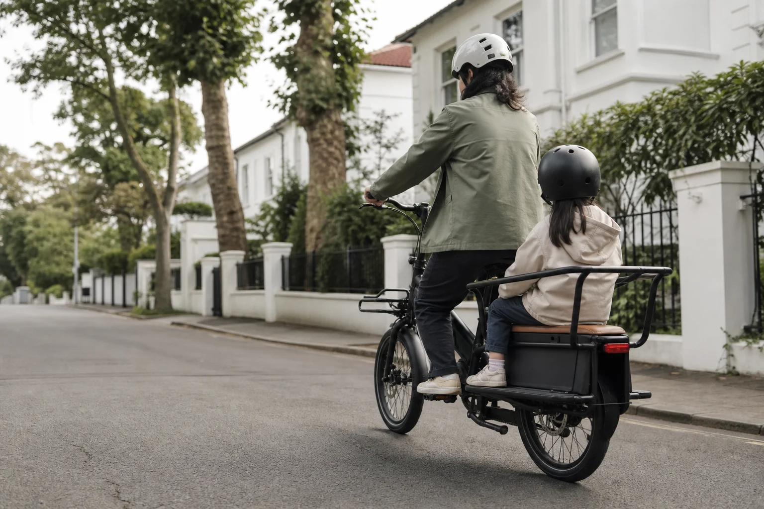 Genitore e figlio su una e-cargo bike mentre pedalano in un quartiere residenziale