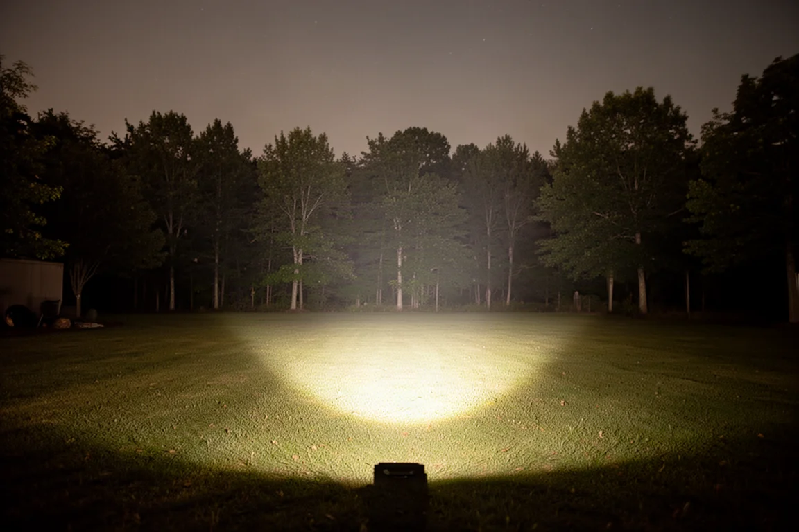 Warm floodlight beam illuminating a backyard tree line at night