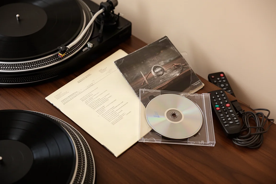 Ovanifrån liggande vy av en skivspelare, ett vinylskivfodral och en cd-skiva på mörkt trä