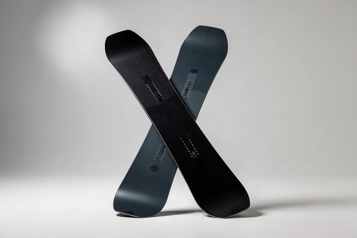 Wide matte black snowboard standing upright on a light grey studio backdrop