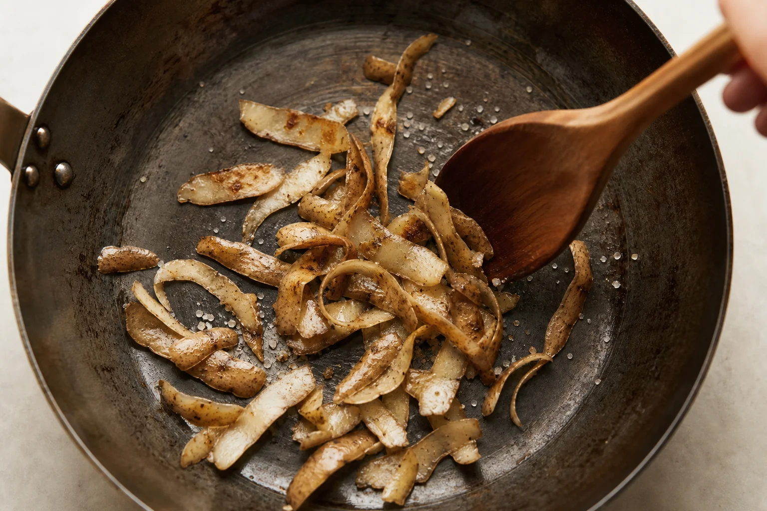 Potato peels and salt in carbon steel pan during seasoning with spotty brown coloring