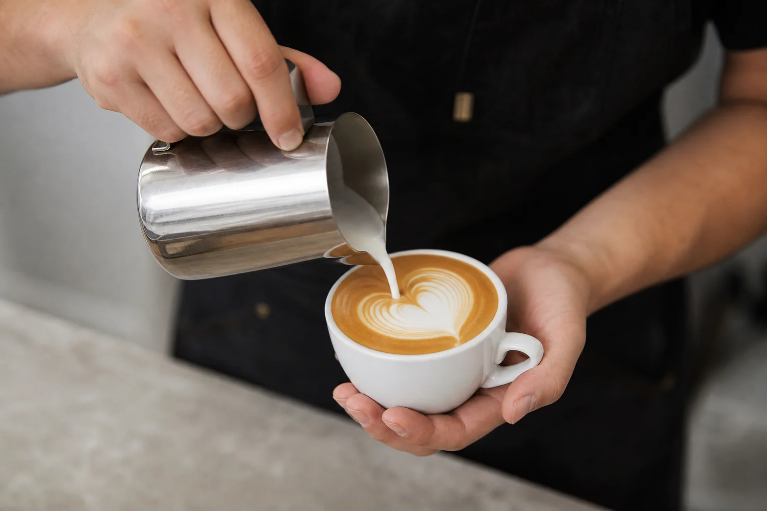 Barista pouring latte art with a milk pitcher into an espresso cup