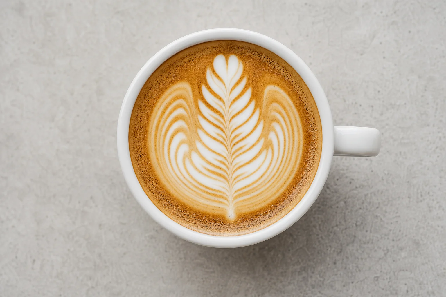 Detailed latte art rosetta pattern in a white espresso cup