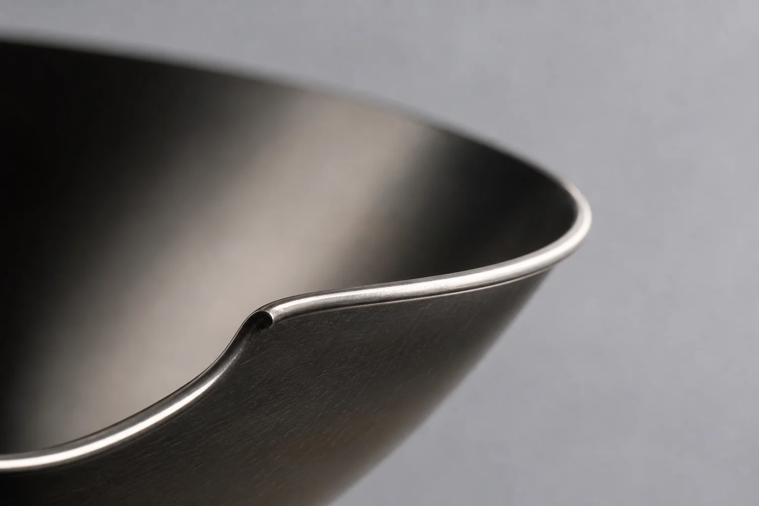 Close-up of a wok's rolled rim edge detail against a neutral backdrop