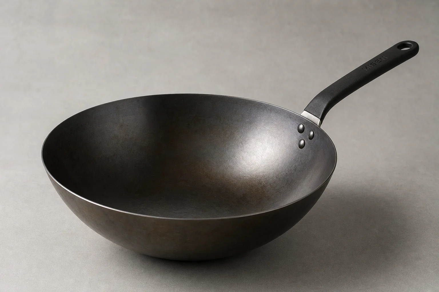 Misen carbon steel wok med mörk inbränd yta mot en neutral bakgrund