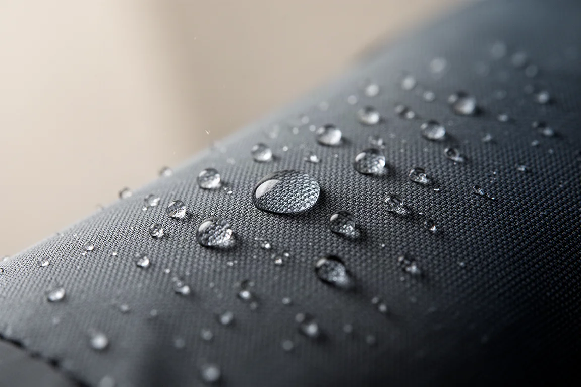 Close-up van water dat parelt en wegrolt van een dun, donker technisch stofoppervlak