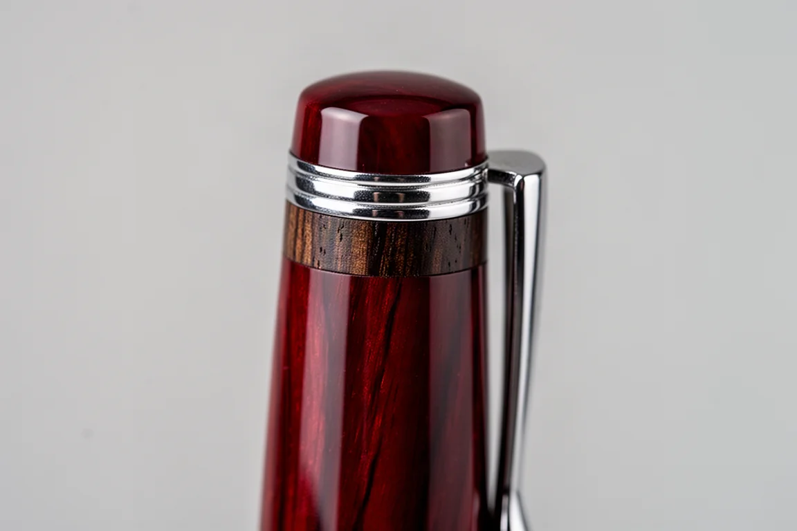 Primo piano del cappuccio di una penna stilografica laccata rossa con anello in legno di noce e clip lucida