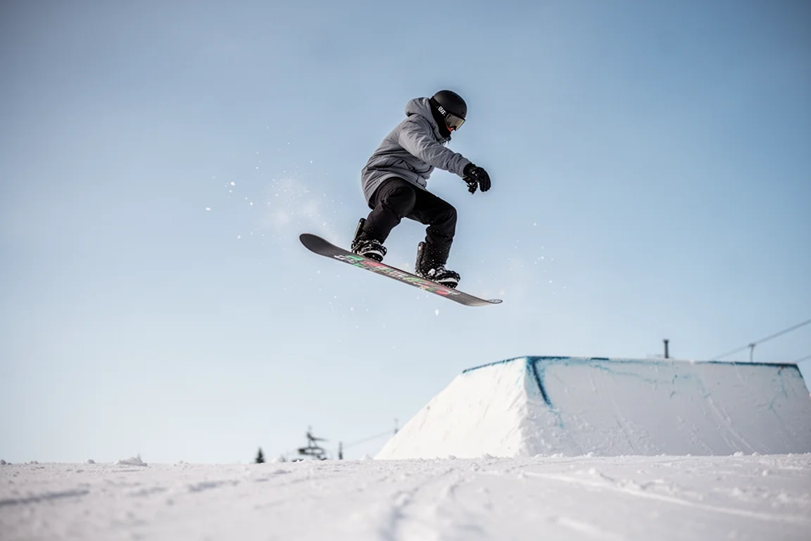 Snowboarder che esegue un ollie da un kicker in stazione sotto un cielo sereno