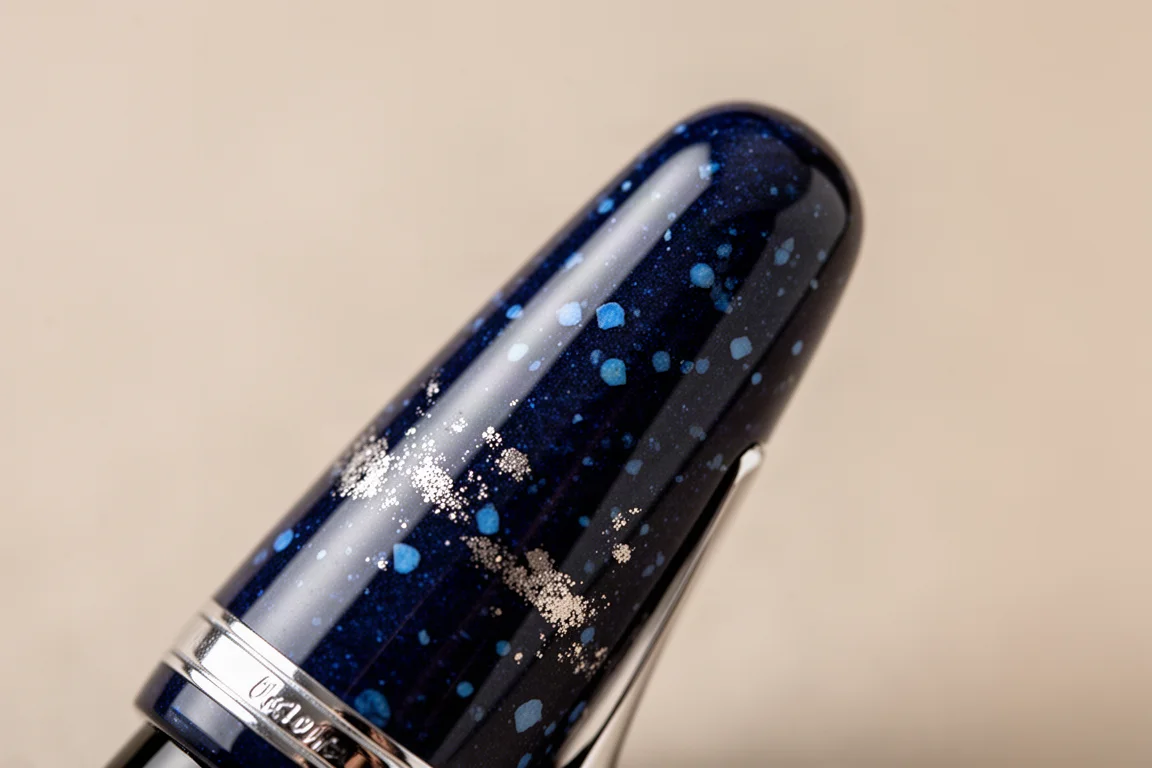 Capuchon du stylo urushi bleu profond montrant la laque mouchetée de platine captant une lumière douce
