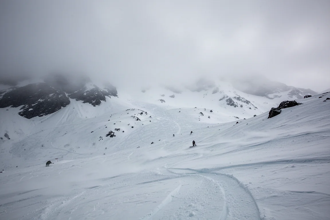 Snowboarder charging through chopped-up fresh snow on an overcast day