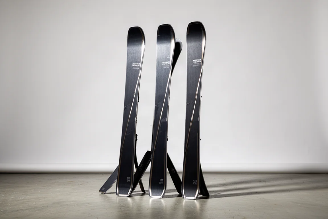 Three pairs of all-mountain skis standing in a row on a concrete floor against a grey backdrop
