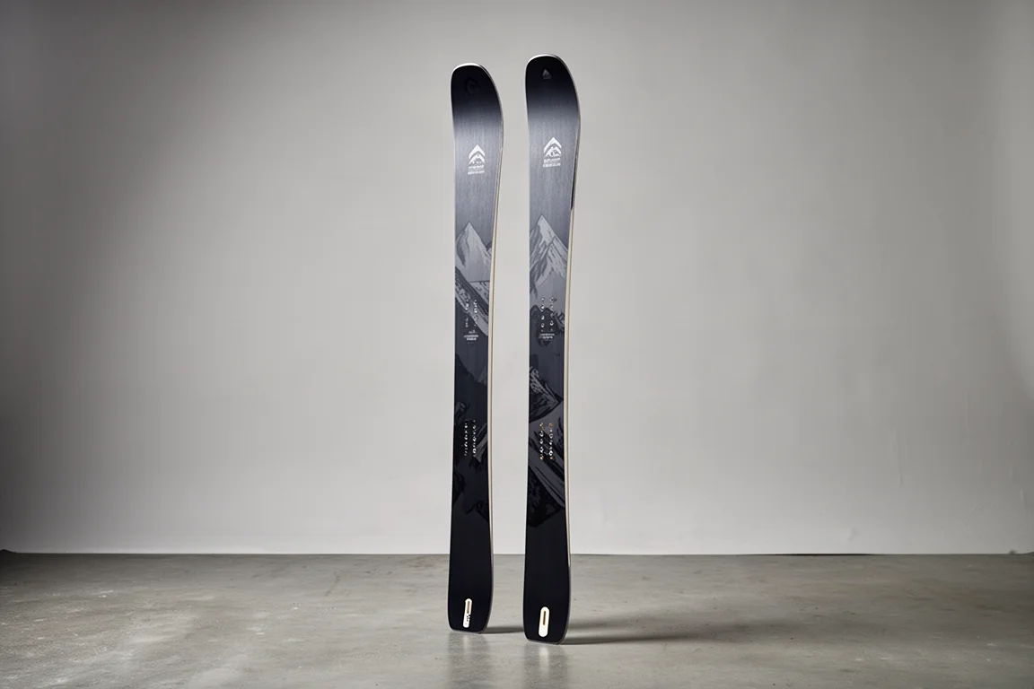 Pair of all-mountain skis standing upright on a matte concrete floor against a grey backdrop