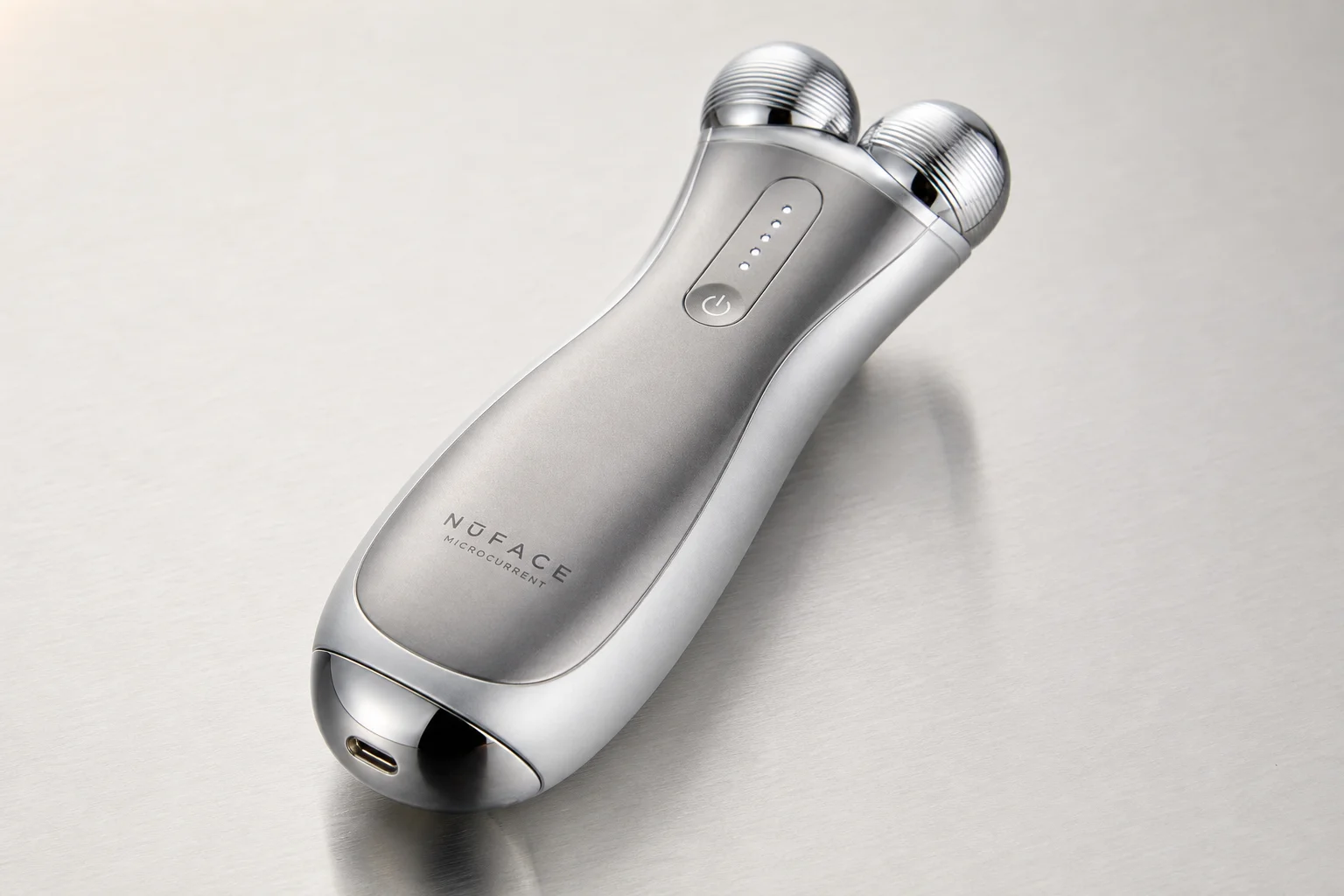 Five anti-aging devices arranged on concrete: gua sha stone, facial patches, microcurrent device, red light mask, and microneedling roller