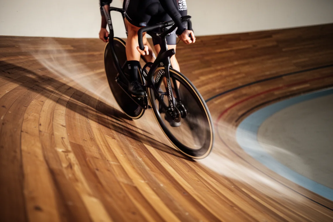 Ciclista de pista inclinando-se em uma curva de velódromo de madeira em alta velocidade