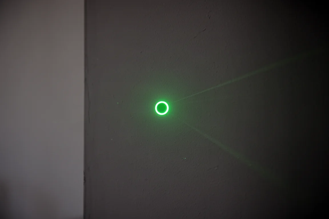 Green laser dot glowing on a wall in a dim room