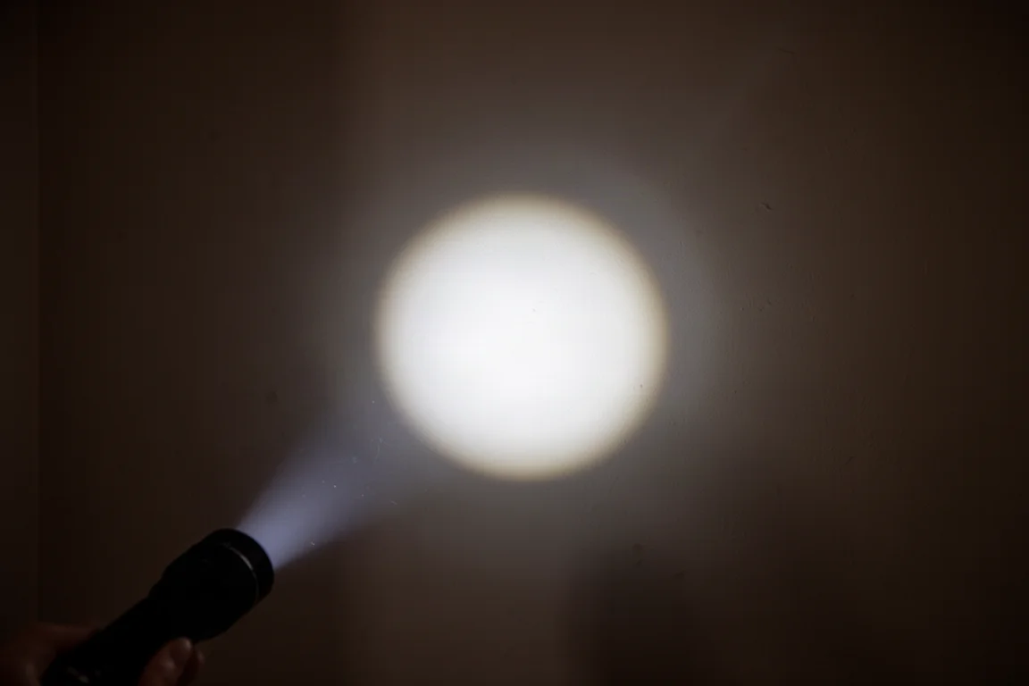 Flashlight beam projecting a tight hotspot on a dark wall