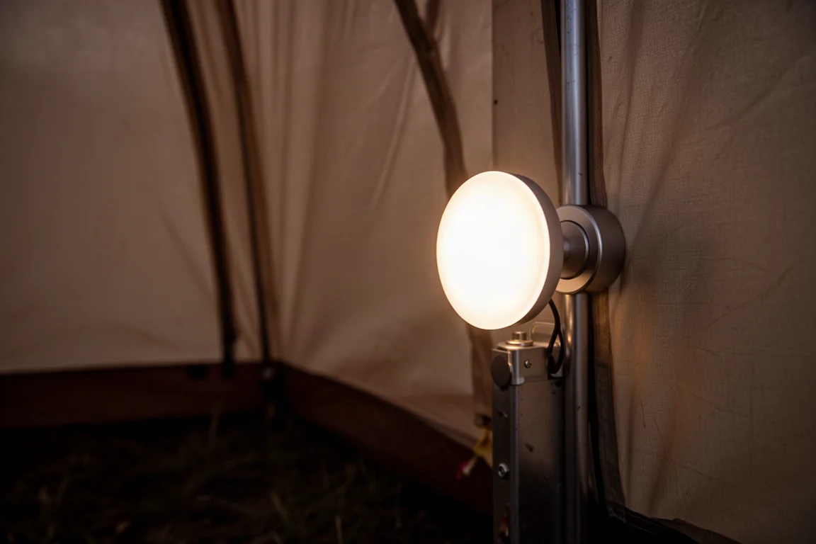 Petite lampe ronde de camping collée à une surface métallique, éclairant l'intérieur d'une tente