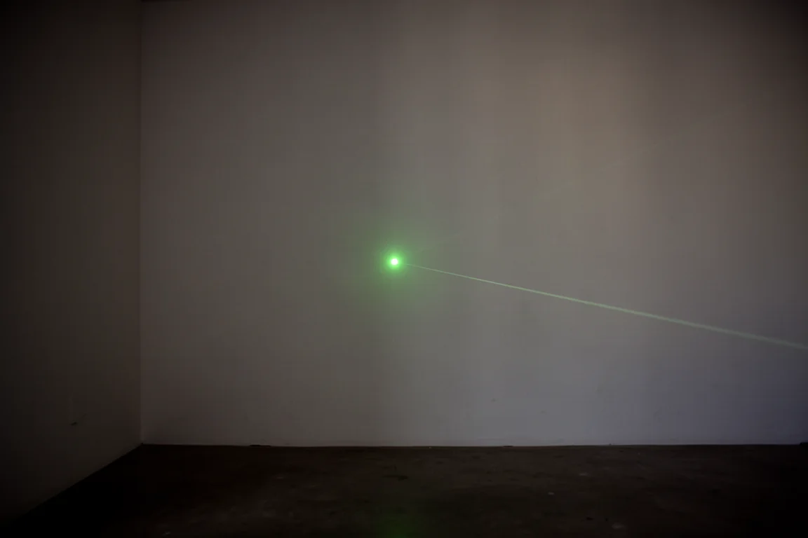 Point vert du laser projeté sur un mur éloigné dans une pièce plongée dans l'obscurité