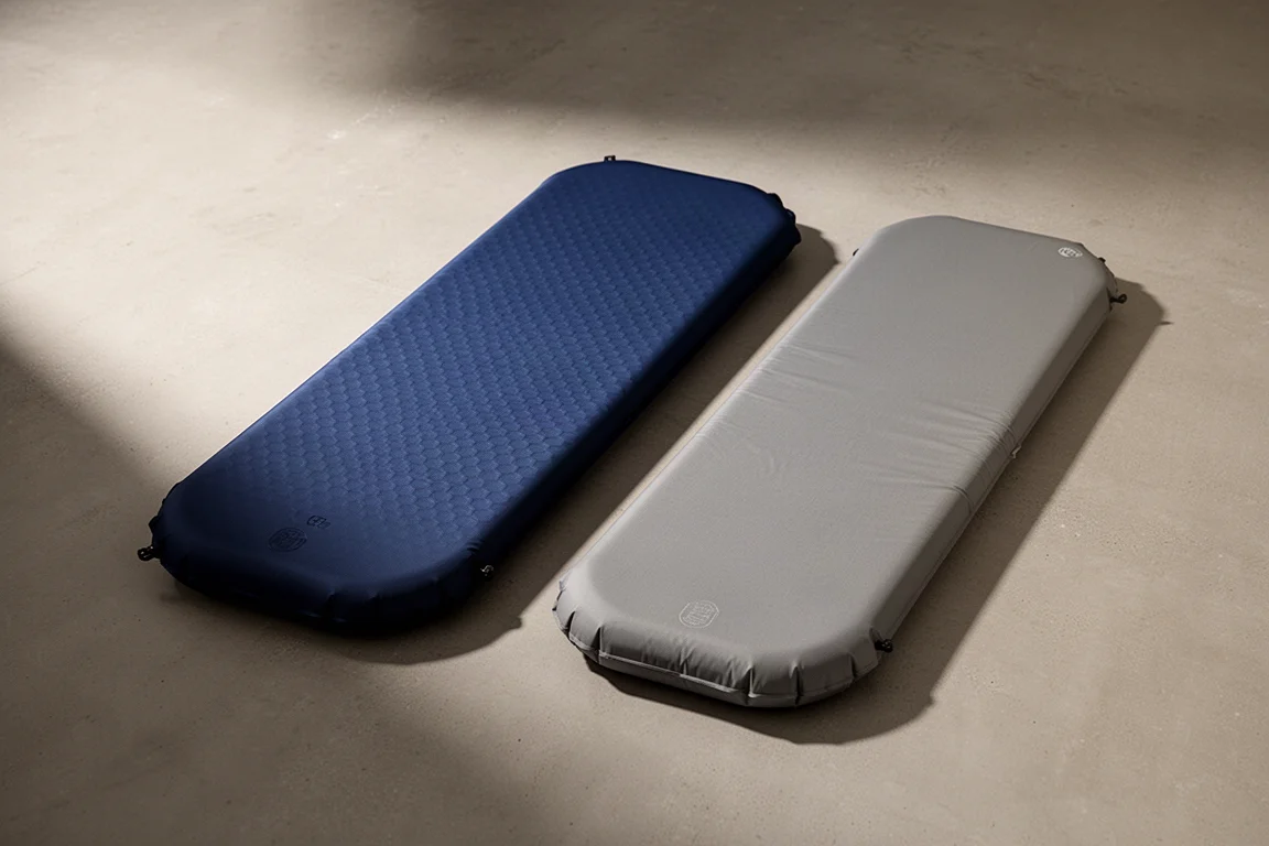 Due materassini da backpacking gonfi, uno blu navy e uno grigio, su una superficie di cemento