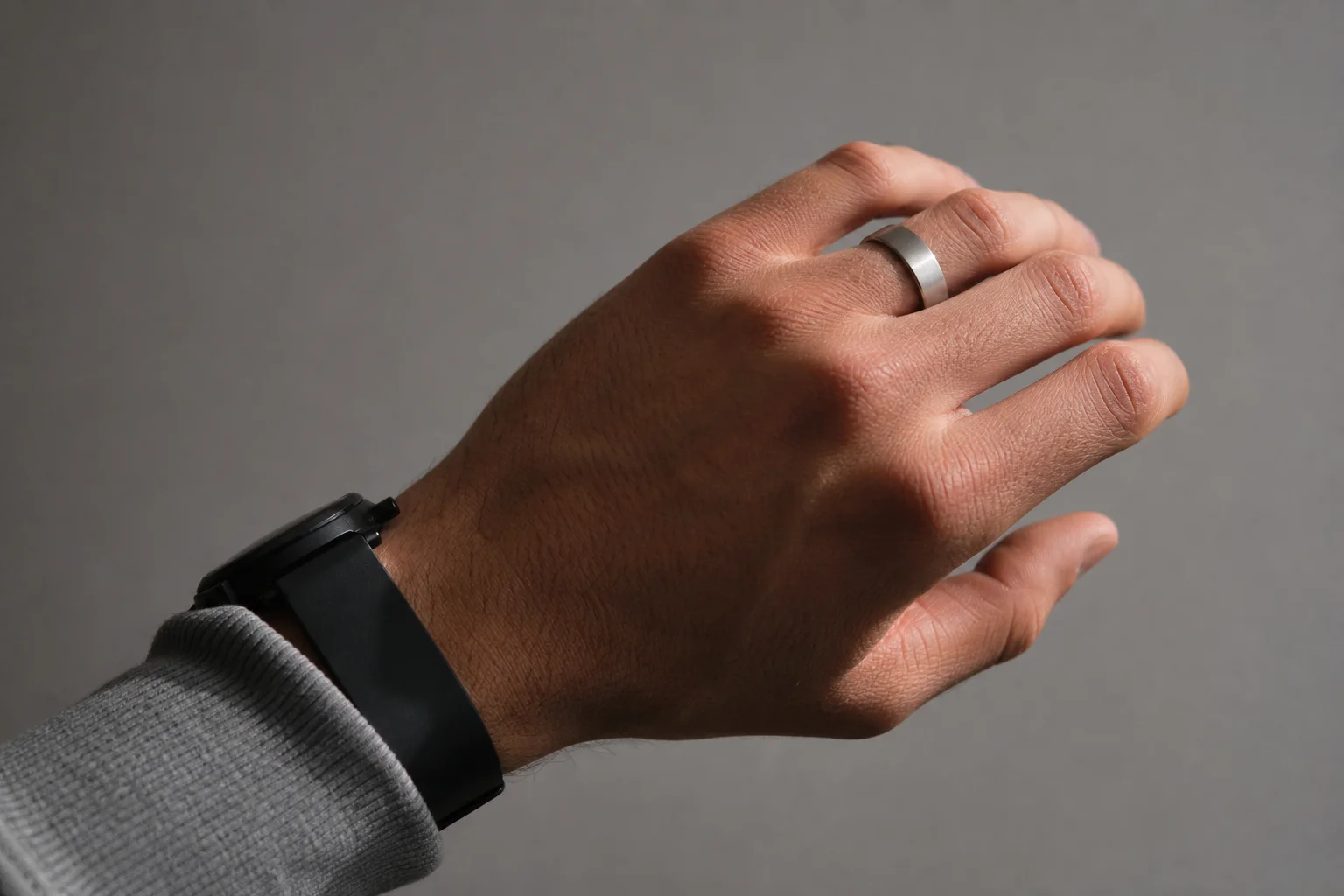 Brushed silver Oura Ring 5 on a finger next to a black watch strap
