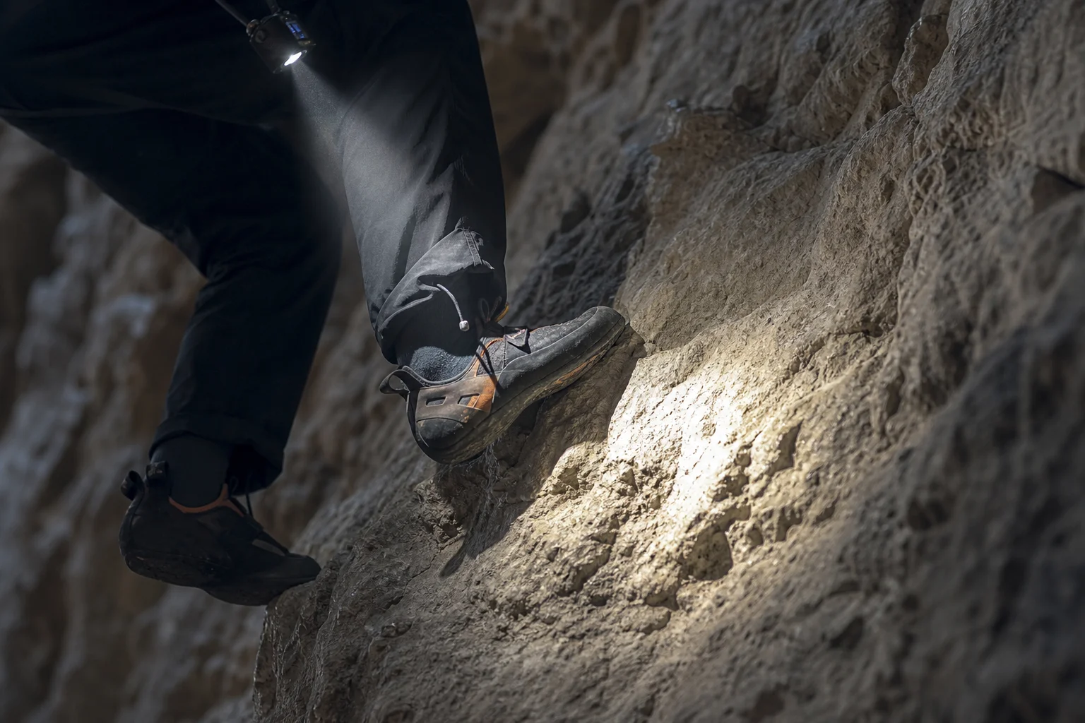 Pieds d'un grimpeur sur une paroi rocheuse éclairée par le faisceau d'une lampe frontale