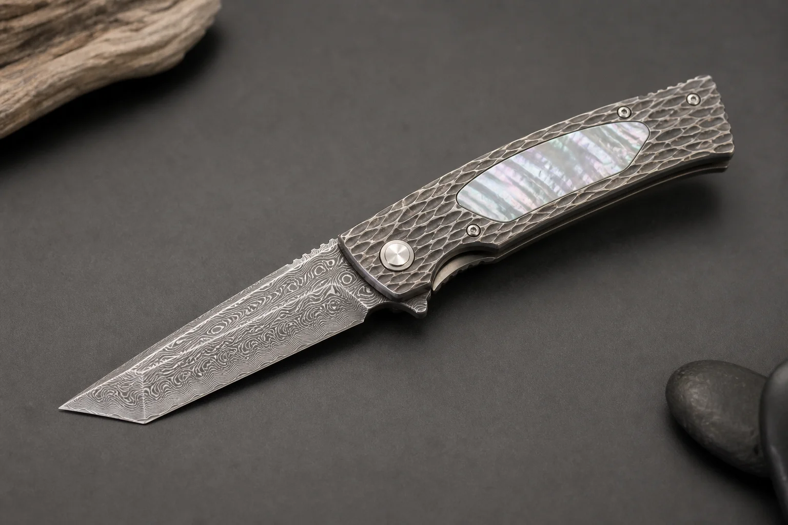 Premium folding knives with titanium handles and Damasteel blades on a dark slate surface