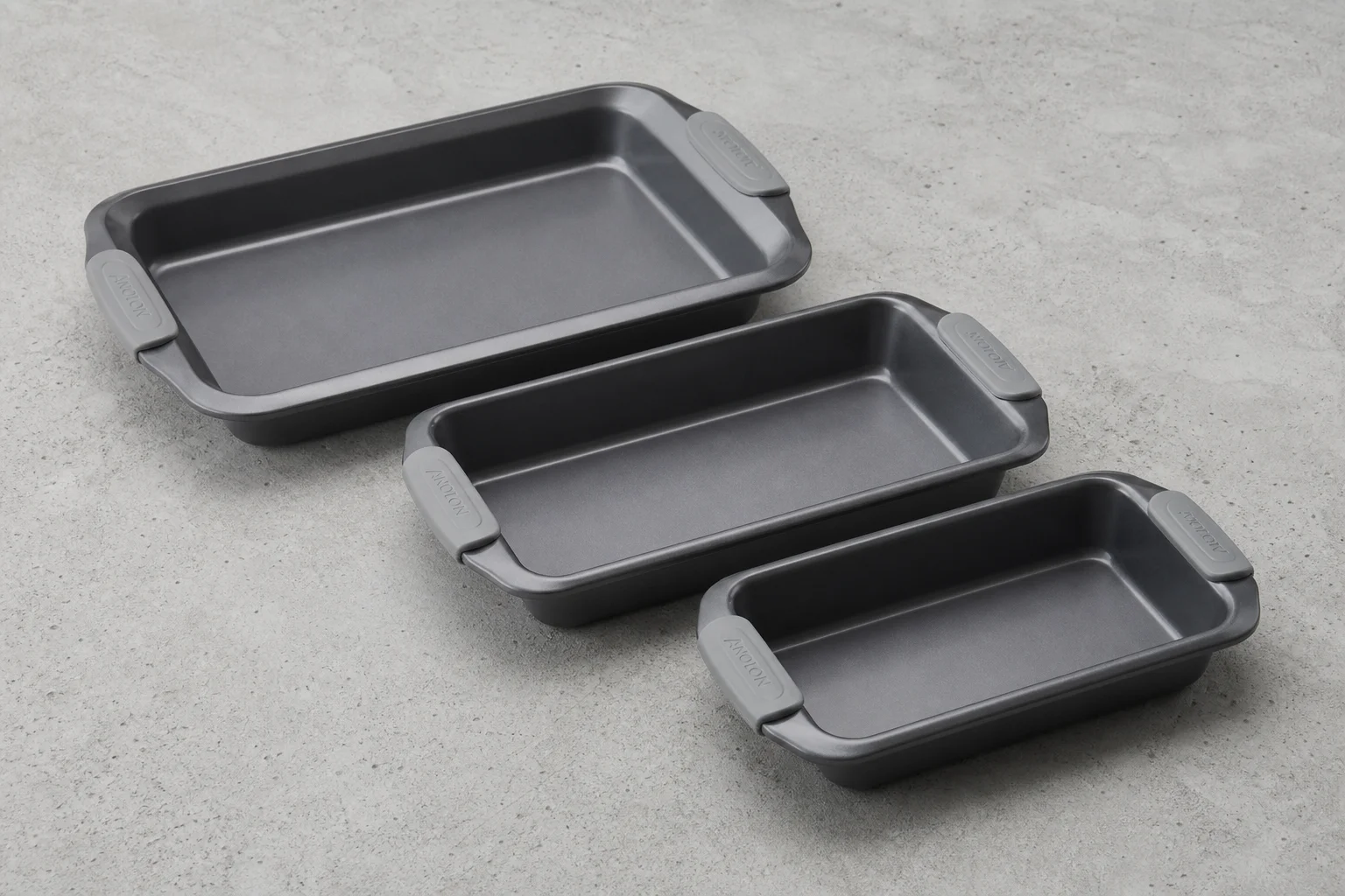 Five different baking sheets and pans arranged on a concrete surface