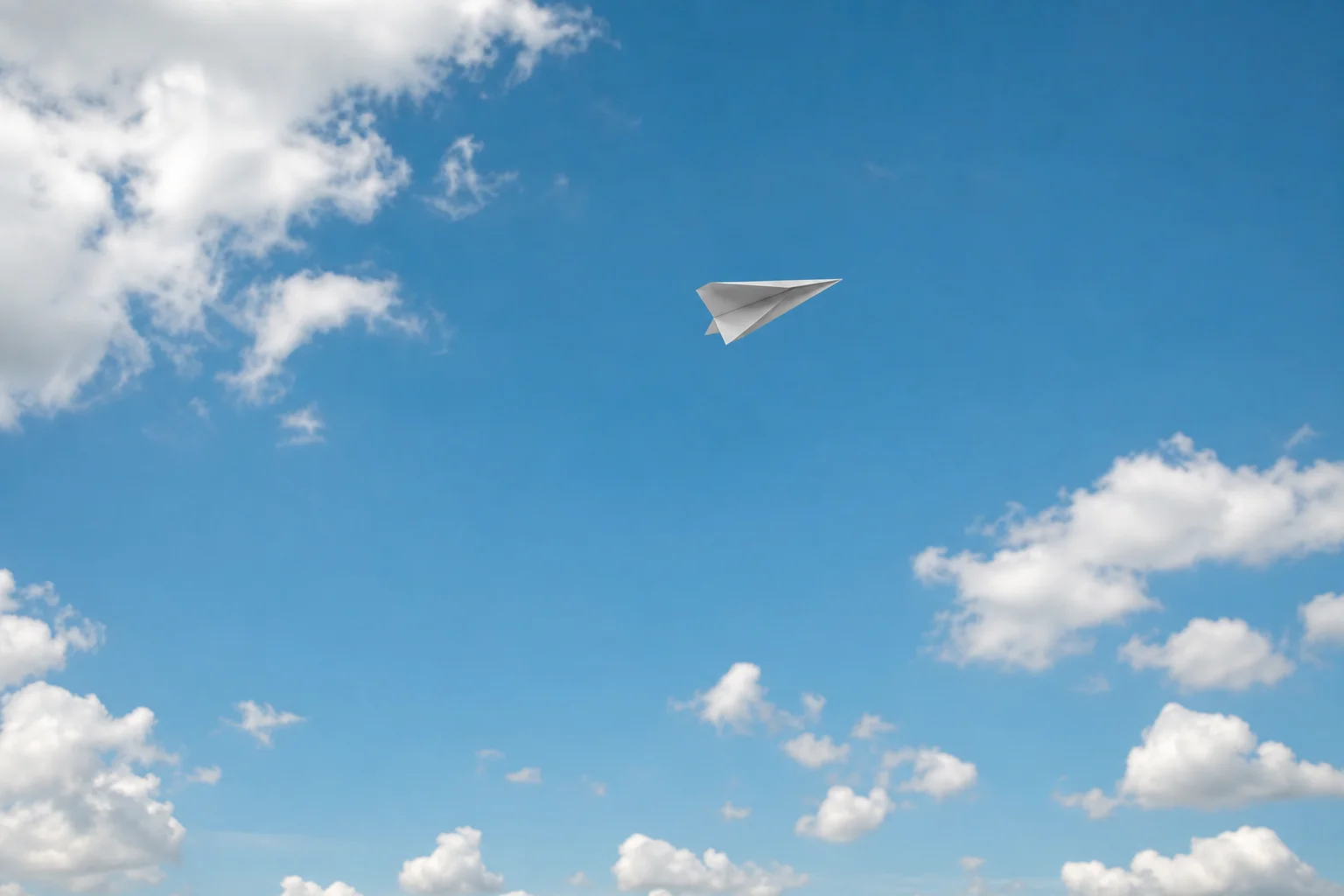 Papierflieger im Flug vor blauem Himmel mit Wolken