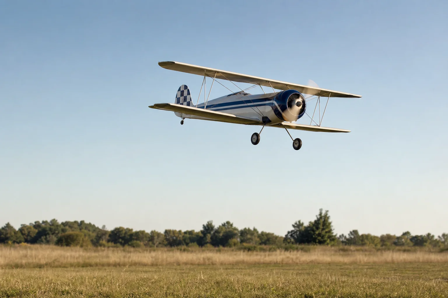 RC-Modell eines Oldtimer-Doppeldeckers im Flug über einem offenen Feld