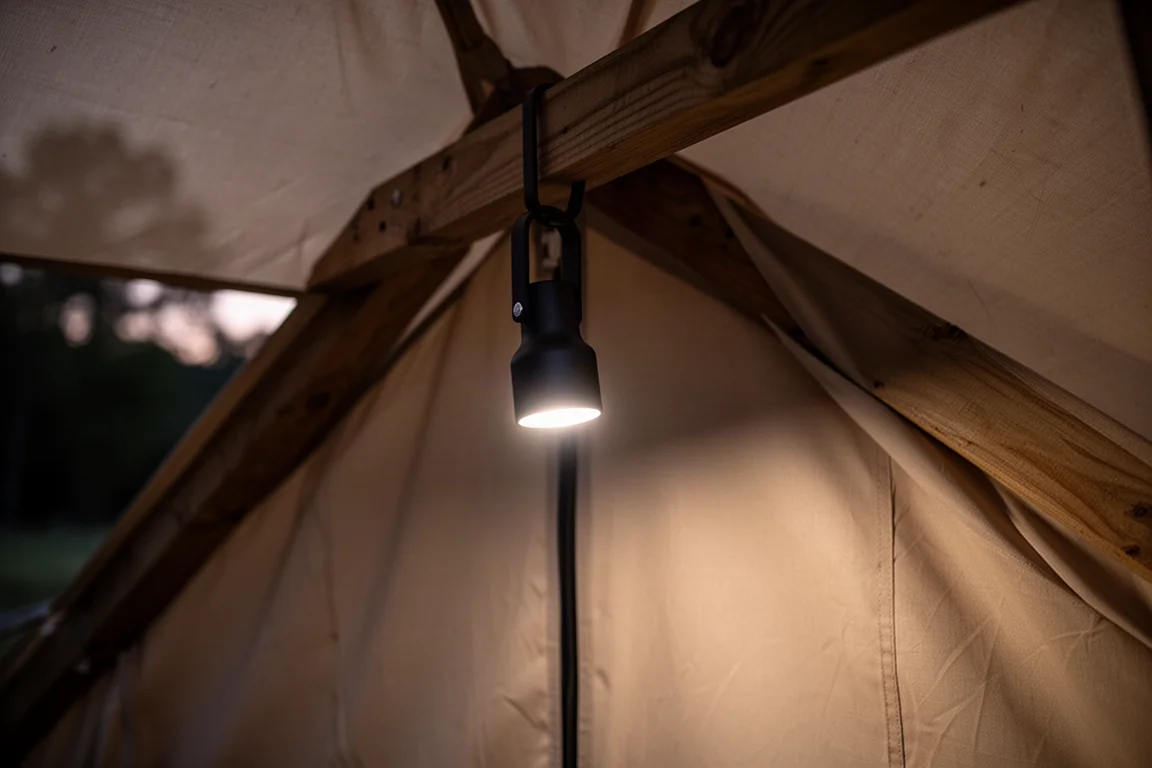 Lampada da lavoro appesa a un gancio su una trave di legno che illumina l'interno di una tenda