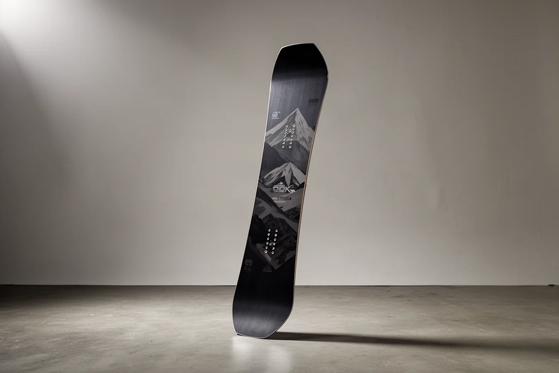Twin-tip all-mountain snowboard som står upprätt på ett matt betonggolv mot en grå bakgrund