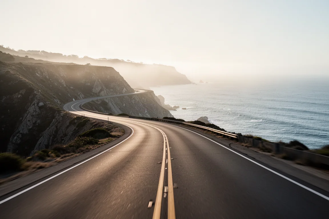 Carretera costera vacía que serpentea entre acantilados sobre el océano bajo una luz dorada